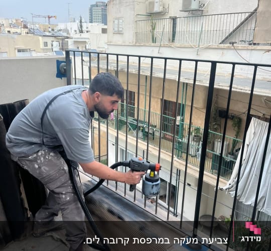 אדם צובע מעקה מתכת עם מכונת ריסוס צבע
